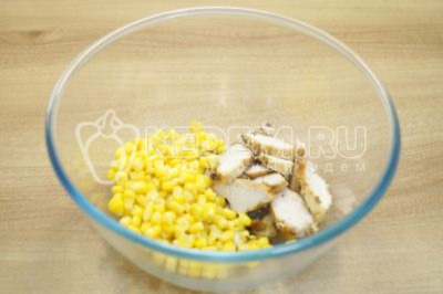 У миску викласти 100 г консервованої кукурудзи та нарізане куряче філе.